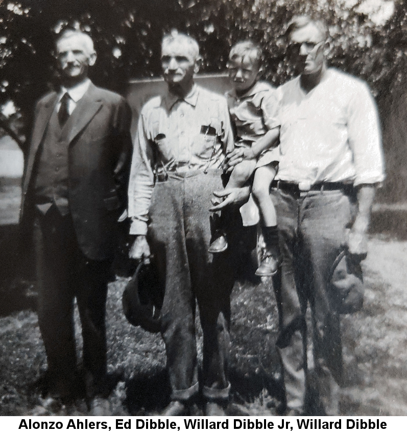 Grey-haired and -moustached Alonzo Ahlers in a three-piece suit, Ed Dibble with thinning grey hair and moustache wearing a work shirt, pocket protectors and pens and work pants, Willard Dibble Sr, in a white shirt with rolled-up sleeves and aviator-style glasses. Ed and Willard are holding Willard Dibble Jr, about 4 years old, in their arms between them.